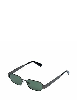 Lunettes de soleil à monture en métal noir avec des verres octogonaux teintés verts et des plaquettes de nez réglables.