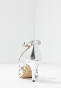 Srebrne metaliczne sandały na wysokim obcasie z paskiem na kostce, odkrytym tyłem, teksturowanym wykończeniem i smukłym obcasem. Rozmiar oznaczony jako 37 na podeszwie.