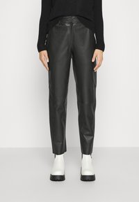 Svarta läderbyxor har en rak ben-design med synliga sömmar och en slät struktur, tillsammans med vita ankelstövlar.