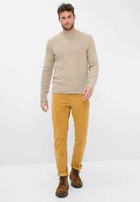 Pull en maille beige mouchetée avec col rond, associé à un pantalon en velours côtelé moutarde et des bottines marron à lacets. Tenue décontractée et texturée.