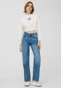 Biały krótki sweatshirt z graficznym nadrukiem, zestawiony z wysokim stanem niebieskich dżinsów. Strój charakteryzuje się luźnym krojem i prostym designem.