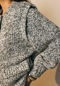 Flauschiger Strickpullover in Grau- und Weißtönen, mit einem strukturierten Muster und umgeschlagenen Bündchen, in einem gemütlichen, übergroßen Schnitt.