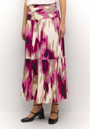 Kvinde iført en lang, højtaljet nederdel med abstrakte mønstre i pink, beige og sort, kombineret med sorte Mary Jane-hæle.