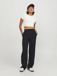 Bílý ribbovaný crop top, černé široké kalhoty s elastickým páskem a bílé tenisky. Doplněno kšiltovkou s maskáčovým vzorem a kroužkovými náušnicemi.