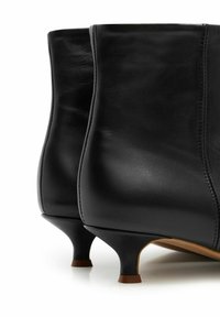 Juodos odinės kulkšnies aulinukai su lygiu paviršiumi, siaurėjančiais aukštais kulnais ir subtiliais siūlės detalėmis. Turi apvalius pirštus ir minimalistinį dizainą.