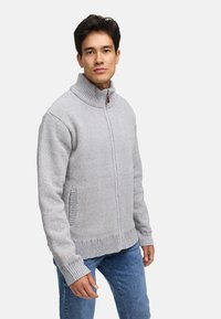 Grå strikket zip-up sweater med høj krave, ribbede manchetter og sidelommer. Blød tekstur med en blanding af lyse og mørke gråtråde.