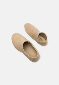 Scarpe slip-on beige con un esterno in similpelle liscia e una parte superiore in pile testurizzato simile a una calza, con punta rotonda e bordi elastici.