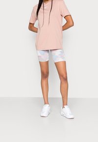 Ljusrosa kortärmad t-shirt i kombination med vita och pastellfärgade camouflagemönstrade cykelshorts med en rosa logotyp, bärs med vita sportskor.