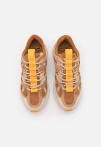 Beiga och bruna sneakers med mesh-överdela, gula accenter, texturerade snören och förstärkt tåhätta. Lättviktsdämpande sula.