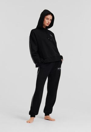 Black hoodie and sweatpants set in cotton blend. Hoodie features a drawstring, while pants have side stripes and a small logo. Smooth texture.