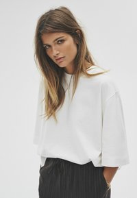 Biała, oversize t-shirt z opadającymi ramionami, w połączeniu z ciemnymi spodniami w paski z elastycznym pasem na sznurku. Gładka tekstura materiału.