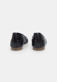 Scarpe in pelle nera con design perforato e bordi scallop, caratterizzate da una suola piatta e una texture liscia.