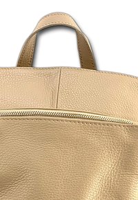 Sac fourre-tout en cuir beige clair avec une surface texturée, des poignées supérieures et une poche zippée à l'avant. Un design simple et fonctionnel.