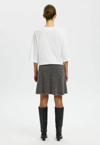 Bijela oversized košulja, siva lepršava suknja i crne kožne čizme do koljena. Glatka tkanina na vrhu, teksturirani materijal na suknji.