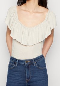 Cremefarvet top med en bred, flæset halsudskæring, korte ærmer og en glat tekstur, parret med højtaljede blå denimjeans.