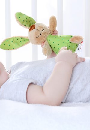 Stuffed rabbit toy with beige fur, green polka-dotted ears and dress, held by a child. Soft texture and rounded features for tactile appeal.