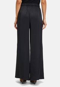 Zwarte wijde broek met een elastische tailleband, gemaakt van een gladde, lichte stof. Heeft een vloeiende silhoutte en geen zichtbare zakken.