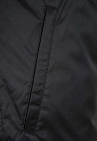 Giacca nera isolante con un tessuto liscio e testurizzato, dettagli con tasca verticale, cuciture pulite e senza loghi o decorazioni visibili.