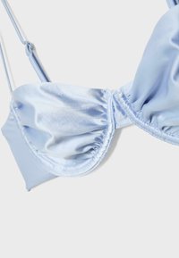Reggiseno di raso azzurro chiaro con coppe arricciate e spalline sottili regolabili su sfondo bianco.