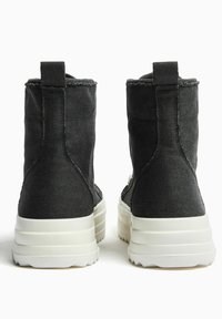 Czarne skórzane botki za kostkę z białymi gumowymi podeszwami, wyposażone w teksturowaną cholewkę, tylne pętelki do ściągania oraz widoczne przeszycia jako akcenty.
