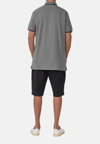 Grijs poloshirt met zwarte accenten, gedragen met zwarte shorts en witte sneakers. Heeft een eenvoudig ontwerp met een klassieke kraag en korte mouwen.
