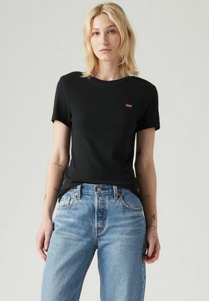 T-shirt en coton noir à manches courtes et col rond, avec un petit logo rouge Levi's sur la poitrine, associé à un jean en denim bleu clair.