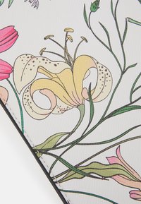 Illustrazione dettagliata di un giglio giallo con accenti rosa, steli e foglie verdi su una superficie bianca testurizzata con cuciture visibili.