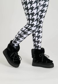 Black faux fur ankle boots with a textured upper, thick sole, and black and white patterned leggings featuring a houndstooth design.