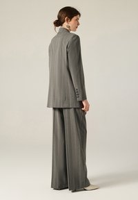 Completo grigio a righe sottili con blazer su misura dotato di colletto alto e pantaloni a gamba larga, entrambi realizzati in un morbido tessuto testurizzato.
