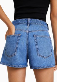 Džínové kraťasy s světle modrým umytím, vysokým pasem a roztrhaným lemem. Obsahují dvě zadní kapsy a viditelné švy.