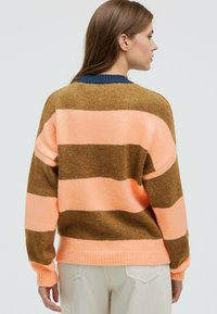 Knit sweater featuring horizontal stripes in brown, light pink, and orange, with a ribbed neckline and hem, and loose, relaxed fit.