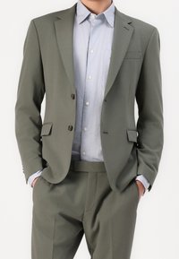 Olivgrön skräddarsydd kostym med enbläddare kavaj, notch-kragar och sidofickor, kombinerad med en ljusblå skjorta med krage under.