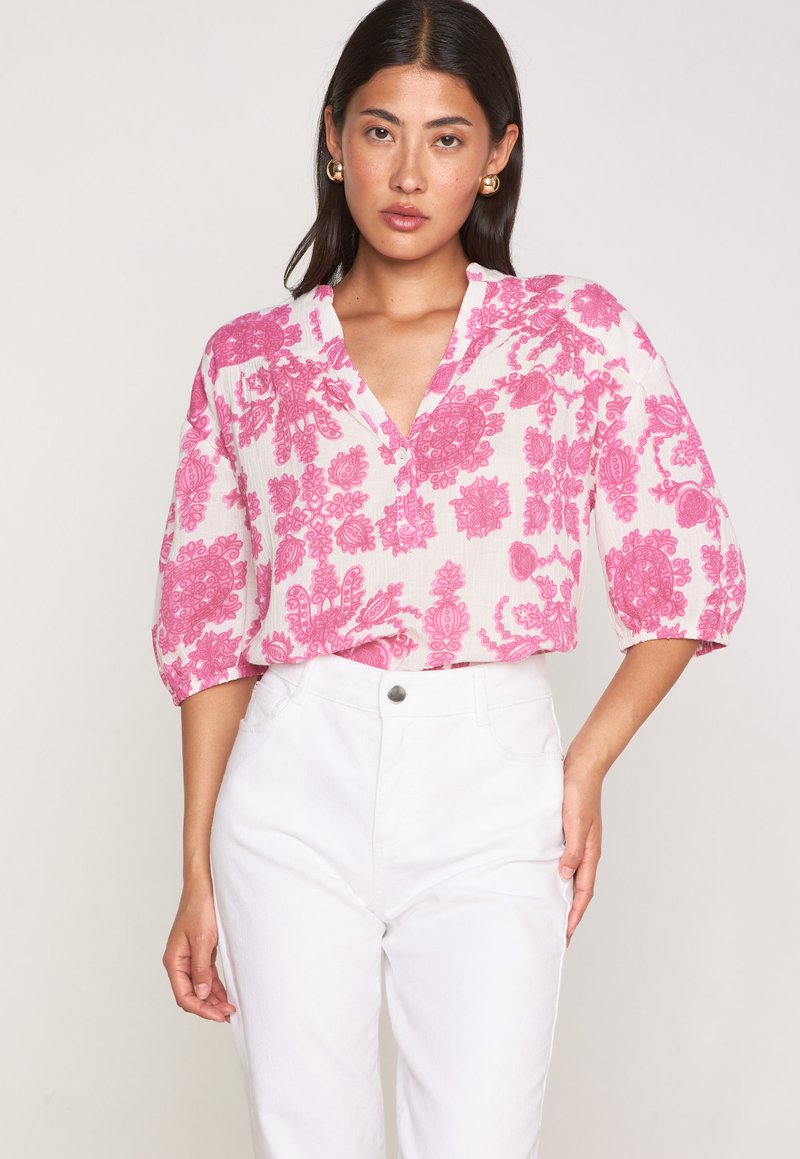 Blusa con motivo floreale in rosa e bianco sporco, con scollatura a V, maniche a tre quarti e una vestibilità ampia. Abbinata a jeans in denim bianchi.