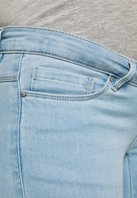 Jeans de mezclilla azul claro con un corte ajustado, costuras visibles y un pequeño bolsillo frontal con detalle de remaches metálicos.