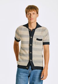 Kortärmad cardigan i cream och grå mesh, med en marinblå ribbad krage, fem knappar och en liten bröstficka.