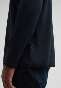 Marineblaues Langarmhemd aus strukturiertem Stoff, mit einer Seitentasche und einer lockeren Passform. Der Saum liegt unterhalb der Taille.