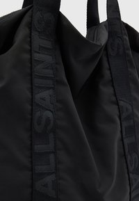 Black nylon tote bag featuring embossed brand logo on straps, smooth texture, and zip closure at the top. Compact and functional design.