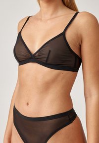 Zwarte mesh bralette met dunne lussen, met een driehoekig ontwerp en zachte textuur. Gecombineerd met bijpassende sheer zwarte high-waisted slipjes.
