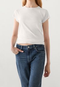 Witte katoenen t-shirt met korte mouwen, ronde hals, gecombineerd met blauwe denim jeans met een voorzak en zichtbare knoopsluiting.