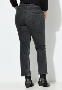 Černé džíny z elastického denimu s vysokým pasem, rovnými nohavicemi a dvěma zadními kapsami. Nošeny s černými kotníkovými botami s ozdobami.