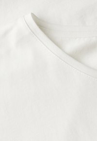 Hvid bomuldsstof med v-hals design. Teksturen er glat med stitched kanter, der fremhæver et minimalistisk æstetik.