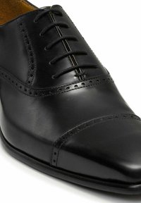 Zwarte leren Oxford herenschoen met gesloten vetersluiting, brogue-details op de kapneus en zijpanelen, gladde gepolijste afwerking.