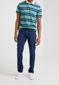 Grön och blå randig polo-shirt med vit krage, ihop med mörkblå jeans och vita sneakers. Inga synliga mönster eller texturer.