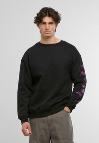 Sort sweatshirt med rund hals, prydet med lilla palmetræ-grafik på venstre ærme. Fremstillet af et blødt, tekstureret stof.