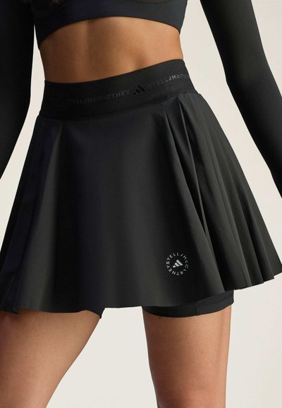 Falda negra plisada con una amplia banda elástica que presenta el logo de la marca, superpuesta sobre pantalones cortos ajustados negros. Tela suave y ligera.