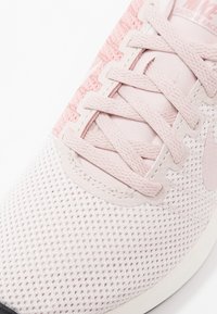 Ljusrosa mesh-sneakers med texturerade överlägg, platta snören och gummisula. Innehåller en subtil Nike-logga i designen.