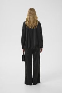 Chándal de satén negro con un diseño holgado, que presenta puños elásticos y rayas laterales, combinado con un pequeño bolso negro estructurado.