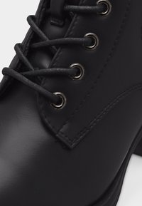 Close-up of black leather boot with round black laces threaded through metal eyelets and detailed stitching.