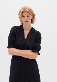 Schwarzes Leinenkleid mit V-Ausschnitt, Puffärmeln und gefransten Manschetten. Glatte Textur und knöchellanges Design mit tailliertem Oberteil.