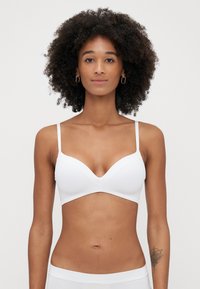 Biały biustonosz wykonany z gładkiego materiału, z głębokim dekoltem, cienkimi regulowanymi ramiączkami oraz bezszwowym wykończeniem. Płaskie, minimalistyczne akcenty.
